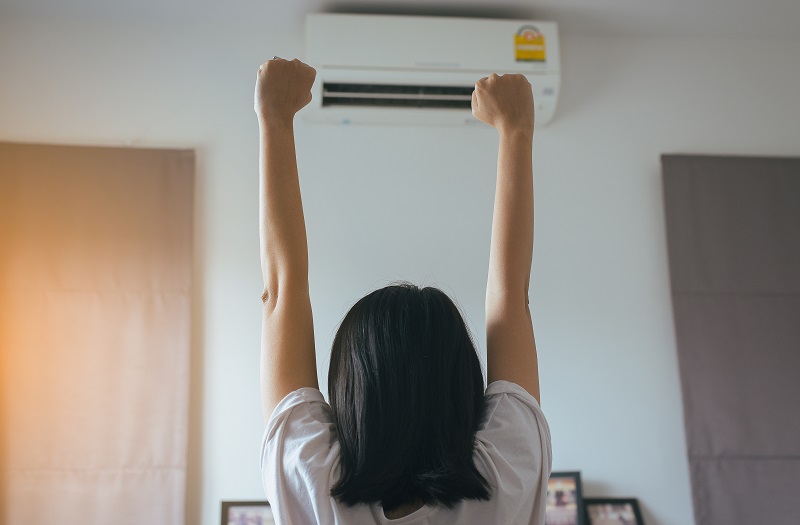 Happy fresh woman hands up and standing in front air conditioner in living room