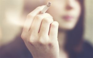 Woman hands holding cigarette outdoor.